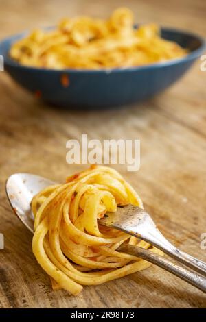 spaghetti all'uovo alla salsa di pomodoro arrotolati su una forchetta con un piatto di spaghetti dello stesso tipo sullo sfondo Foto Stock