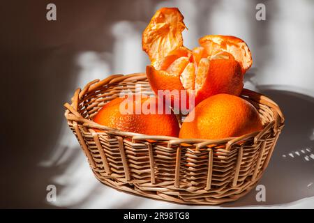 Primo piano di un cestello in tessuto con tre mandarini nella luce tenue della finestra. Foto Stock