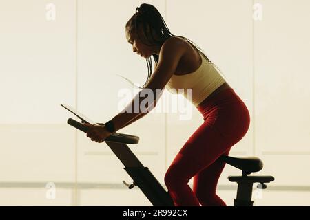 Donna in forma, vestita di abbigliamento sportivo, pedala su una cyclette nella sua routine di allenamento in palestra. Giovane donna che dimostra il suo impegno nel mantenere Foto Stock