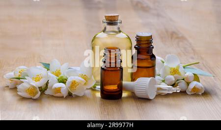 Fiori di gelsomino bianco con foglie verdi e bottiglie di vetro con olio essenziale Foto Stock