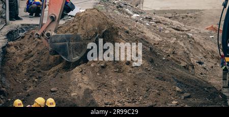 Retroescavatore che opera scavando il terreno in cantiere. Denti della benna del retroescavatore per lo scavo di sabbia. Escavatore cingolato che scava sul terreno. Macchina da scavo. Foto Stock
