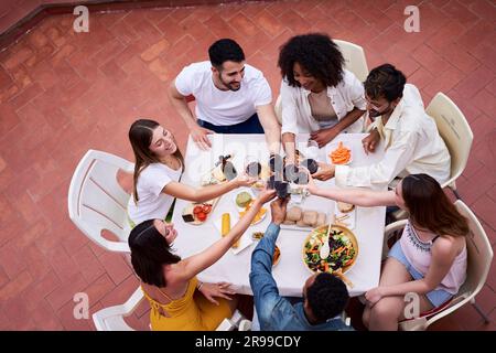 Vista dall'alto di un felice gruppo di amici che brindano con vino rosso all'aperto in una terrazza per festeggiare. Foto Stock