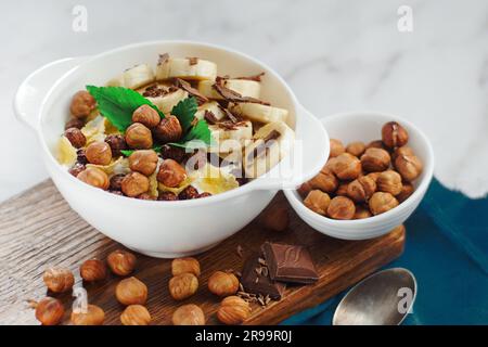 Macedonia di frutta con nocciole, banana e menta in un piatto bianco. Foto pubblicitaria. Vista dall'alto. La colazione era molto utile. Foto Stock