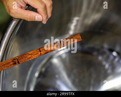 Mano con bastoncino di legno per diluire il sake con acqua, per regolare il livello di alcol. Akashi, prefettura di Hyogo, Giappone. Foto Stock