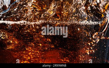 Cola con ghiaccio. Primo piano dei cubetti di ghiaccio nell'acqua cola. Consistenza di bevanda carbonatica con bolle in vetro. Cola soda e schizzi di ghiaccio che fischiano o galleggiano Foto Stock