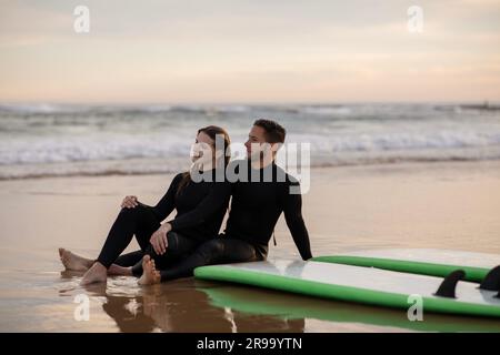 Una giovane coppia felice che si rilassa sulla spiaggia dopo aver fatto surf Foto Stock