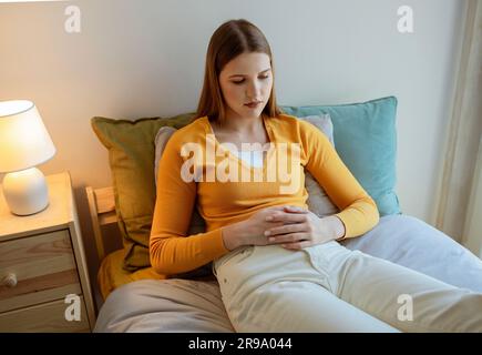 Giovane bionda signora che soffre di dolore mestruale periodo in camera da letto Foto Stock