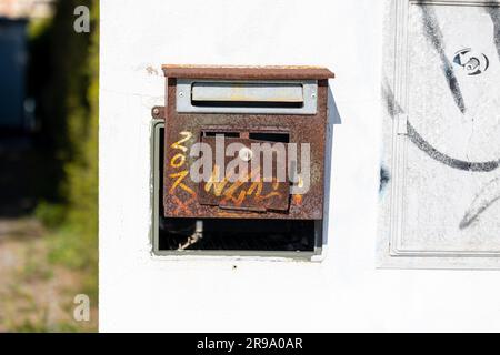 Una vecchia cassetta postale di metallo arrugginita fissata a una parete bianca in condizioni difficili, che mostra anni di usura Foto Stock