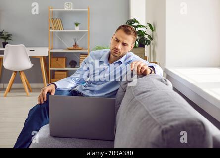 Giovane uomo d'affari serio seduto sul divano, che usa un notebook e pensa Foto Stock