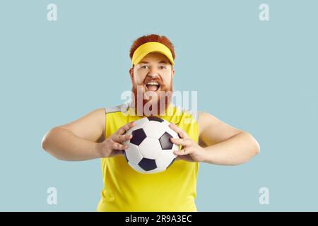 Ritratto di un uomo grasse con la barba, felice eccitato, divertente e barbuto, che tiene la palla da calcio e urla Foto Stock