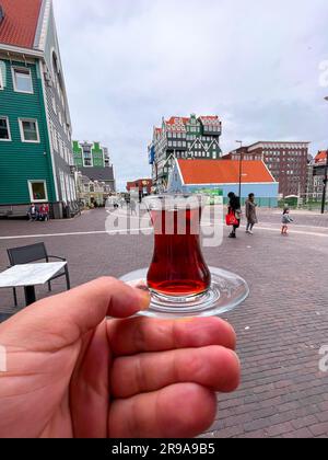 Zaandam, Paesi Bassi - 13 ottobre 2021: Mano dell'uomo che tiene il tè turco contro l'iconico edificio dell'Inntel Hotel Zaandam a Zaandam, il Nether Foto Stock