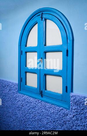 Un muro esterno e una finestra ad arco in legno sono in tre tonalità di blu, ben rappresentative della città Blu, Chefchaouen, Marocco Foto Stock