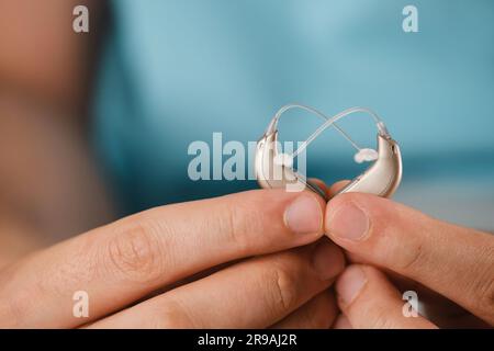 Gli apparecchi acustici nelle mani creano una forma a cuore su sfondo blu. Primo piano dell'apparecchio di ascolto per le persone con disturbi dell'udito, disfunzione. Tecnologia Foto Stock