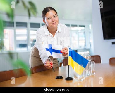 Lavoratrice d'ufficio che mette bandiere di Finlandia e Ucraina sul tavolo negoziale Foto Stock