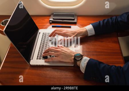 Primo piano irriconoscibile elegante dirigente d'affari che lavora su un moderno computer portatile in un aereo privato di prima classe, Side View Foto Stock