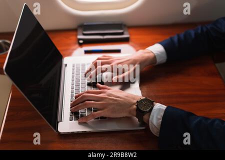 Primo piano irriconoscibile elegante dirigente d'affari che lavora su un moderno computer portatile in un aereo privato di prima classe, Side View Foto Stock