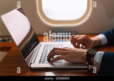 Primo piano irriconoscibile elegante dirigente d'affari che lavora su un moderno computer portatile in un aereo privato di prima classe, Side View Foto Stock