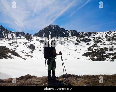 Un adulto sorridente vestito con attrezzatura da sci si trova sulla neve, godendosi la pittoresca vista delle montagne Foto Stock