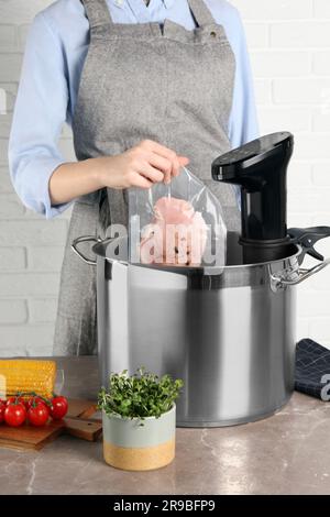 Donna che mette la carne sottovuoto impaccata in pentola con cucina sous vide, primo piano. Circolatore a immersione termica Foto Stock