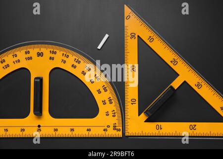 Goniometro, righello triangolare e gesso su tavolo nero, piatto Foto Stock