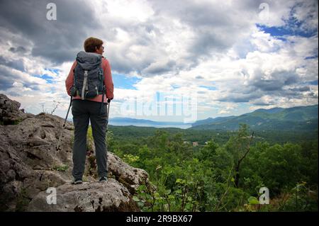 Vista posteriore della donna anziana in piedi al bordo di una scogliera in montagna Foto Stock