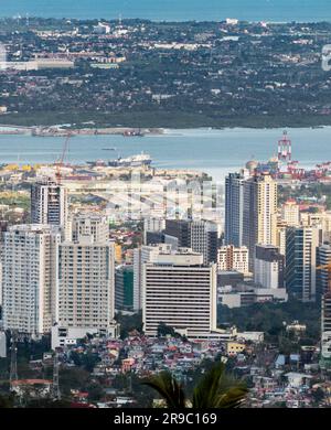 Prima del tramonto la luce del sole bagna gli edifici più alti della capitale di Cebu, guardando attraverso il canale del mare fino all'Isola di Maktan, sopra le palme e il lussureggiante fogliame Foto Stock