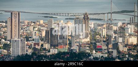 Prima del tramonto la luce del sole bagna gli edifici più alti della capitale di Cebu, guardando attraverso il canale del mare fino all'Isola di Maktan, sopra le palme e il lussureggiante fogliame Foto Stock