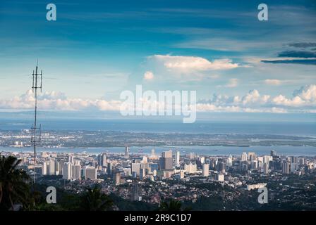 Prima del tramonto la luce del sole bagna gli edifici più alti della capitale di Cebu, guardando attraverso il canale del mare fino all'Isola di Maktan, sopra le palme e il lussureggiante fogliame Foto Stock