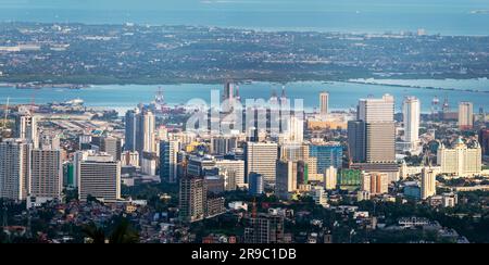 Prima del tramonto la luce del sole bagna gli edifici più alti della capitale di Cebu, guardando attraverso il canale del mare fino all'Isola di Maktan, sopra le palme e il lussureggiante fogliame Foto Stock