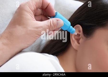 Uomo anziano che gocciola il farmaco nell'orecchio della donna sul divano, primo piano Foto Stock