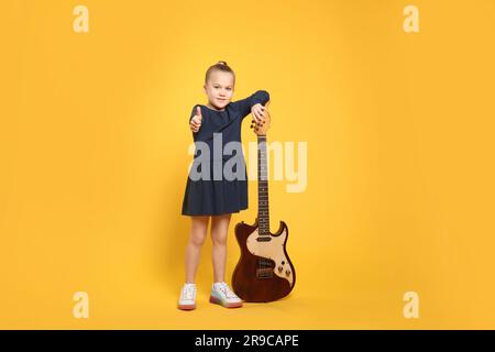 Ragazza felice con chitarra elettrica su sfondo giallo Foto Stock