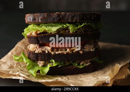 Delizioso sandwich con tonno, pomodori e lattuga su tavola nera, primo piano Foto Stock