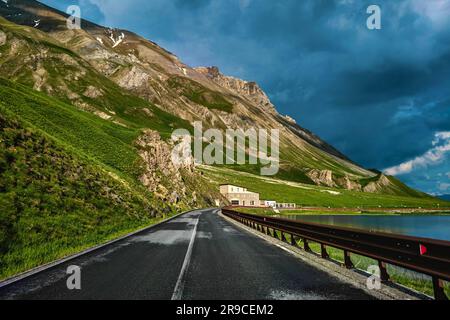 Strada tra piccolo lago alpino e montagne sotto il cielo torbido e torbido vicino al Colle della Maddalena in Italia. Foto Stock