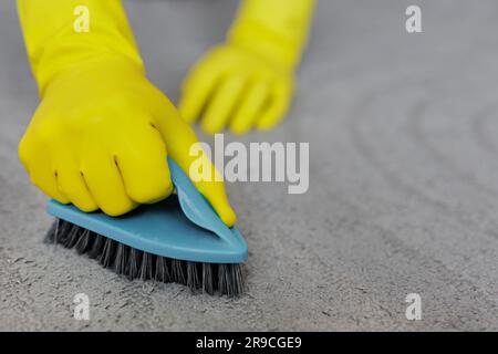 concetto di pulizia - primo piano delle mani in guanti di gomma gialli per la pulizia di tappeti grigi con spazzola Foto Stock