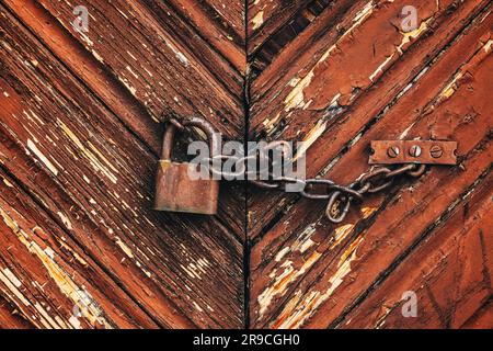 Un vecchio lucchetto corroso e arrugginito con catena su una porta in legno della fattoria come sfondo Foto Stock