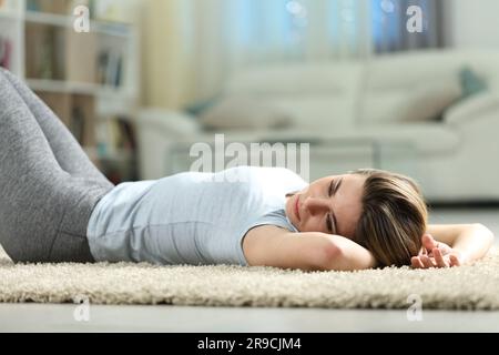 Donna triste sdraiata su un tappeto scoraggiata a casa di notte Foto Stock