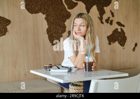 Una donna preoccupata siede nel bar e sembra ben lontana dalla finestra Foto Stock