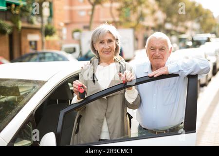 Donna matura e uomo in piedi accanto all'auto, donna che tiene le chiavi in mano. Foto Stock