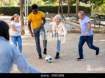 La squadra di calcio composta da persone diverse di età positiva e di mezza età che trascorrono del tempo insieme e svolgono attività in un'area sabbiosa Foto Stock