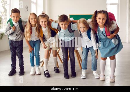 Un gruppo di bambini sorridenti e con zaini che si aggrappano in classe Foto Stock