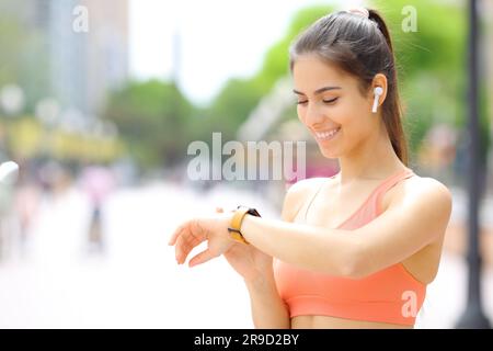 Happy runner che indossa gli auricolari per selezionare la musica sullo smartwatch prima di correre in strada Foto Stock