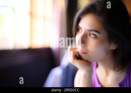 Donna pensiva che si rilassa guardando dalla finestra seduta a casa Foto Stock