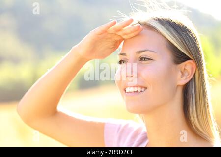 La donna felice con la mano sulla fronte protegge dal sole in natura Foto Stock