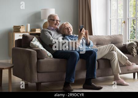 Coppia matura e felice che usa il cellulare per rilassarsi insieme sul divano Foto Stock