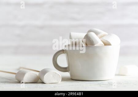 Marshmallow bianchi in una tazza bianca su sfondo bianco con spazio per la copia. Foto Stock