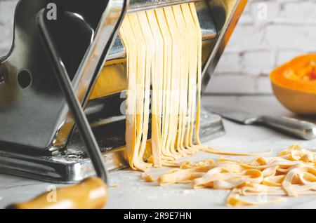 Tagliatelle di zucca in una macchina per la pasta, un coltello e un pezzo di zucca di burro, su fondo di marmo. Foto Stock