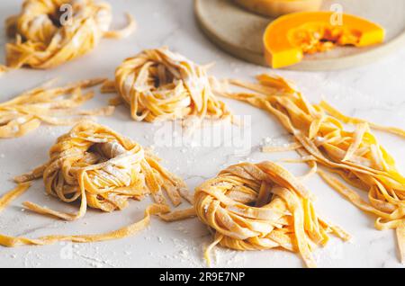 Nidi di tagliatelle di zucca e alcune fette di zucca in un piatto, su fondo di marmo. Foto Stock