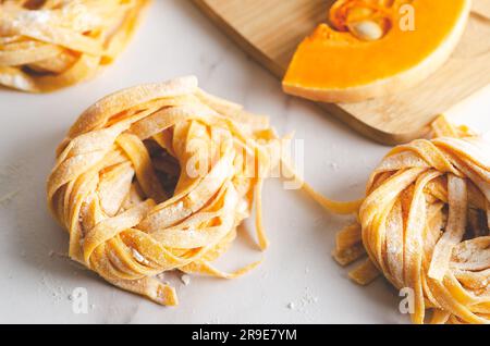 Nidi di tagliatelle di zucca e una fetta di zucca su una tavola di legno su fondo di marmo. Foto Stock