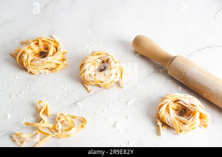 Nidi di tagliatelle da squash Butternut e un mattarello su sfondo marmo. Foto Stock