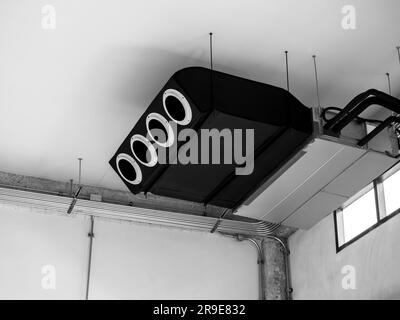 Macchina nera, aria condizionata moderna, sistema di ventilazione a soffitto decorato sul soffitto vicino al cablaggio elettrico tubi in acciaio in vecchio bianco Foto Stock